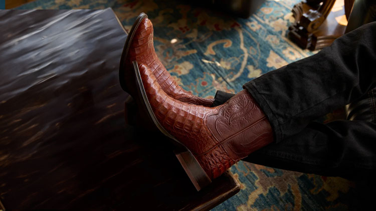 A man sitting on a couch with his feet up wearing a pair of Tony Lama boots.